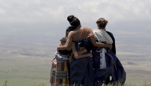 Three women arm in arm looking out over the plains of Hawai‘i.