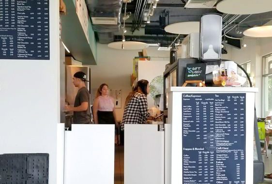 behind the counter at a cafe with menu board and employees working