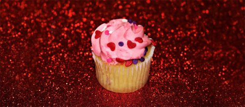 Vanilla cupcake with pink frosting on red glitter covered surface