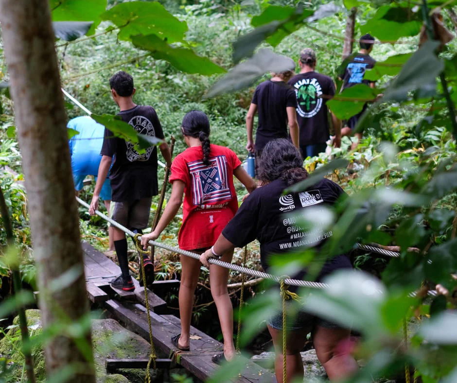 High school students walking on a rope bridge in the forest.